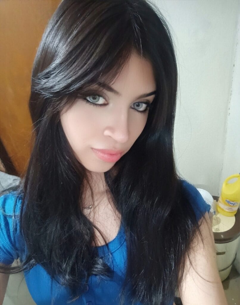 Close-up portrait of a young woman with long dark hair and blue-green eyes looking at the camera.